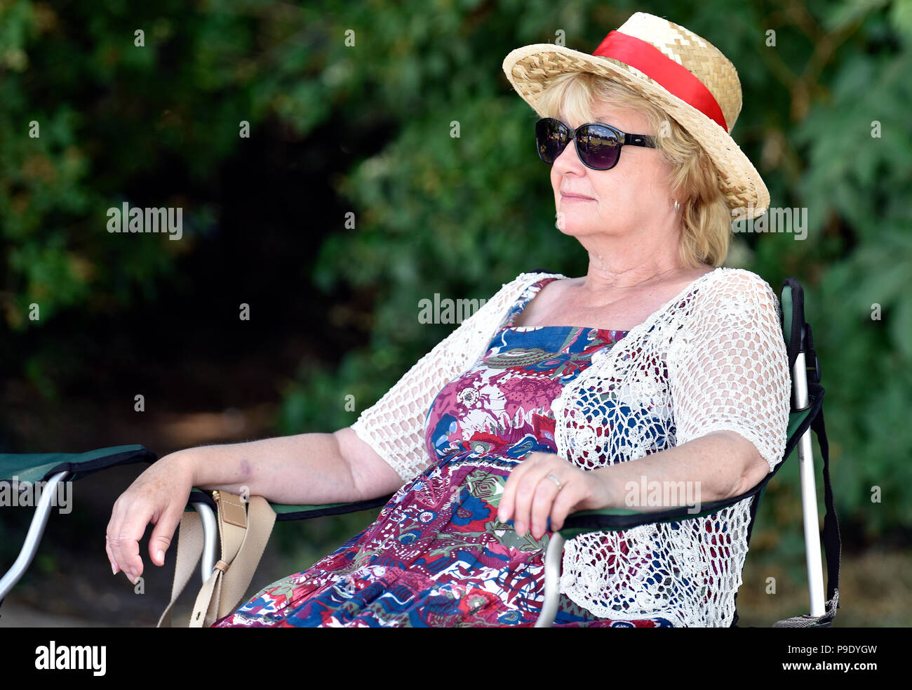 Ältere Frau an einer Bushaltestelle rally Entspannen im Warmen, Sommer Sonnenschein, Alton, Hampshire, UK. Sonntag, 15. Juli 2018. Stockfoto