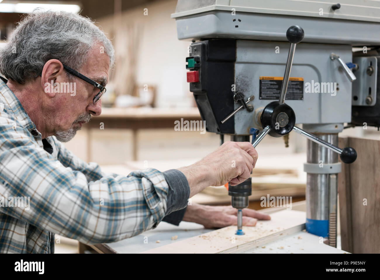 Ein älterer Mann mit Brille und Bart in einem holzarbeiter Shop, mittels einer Maschine. Stockfoto