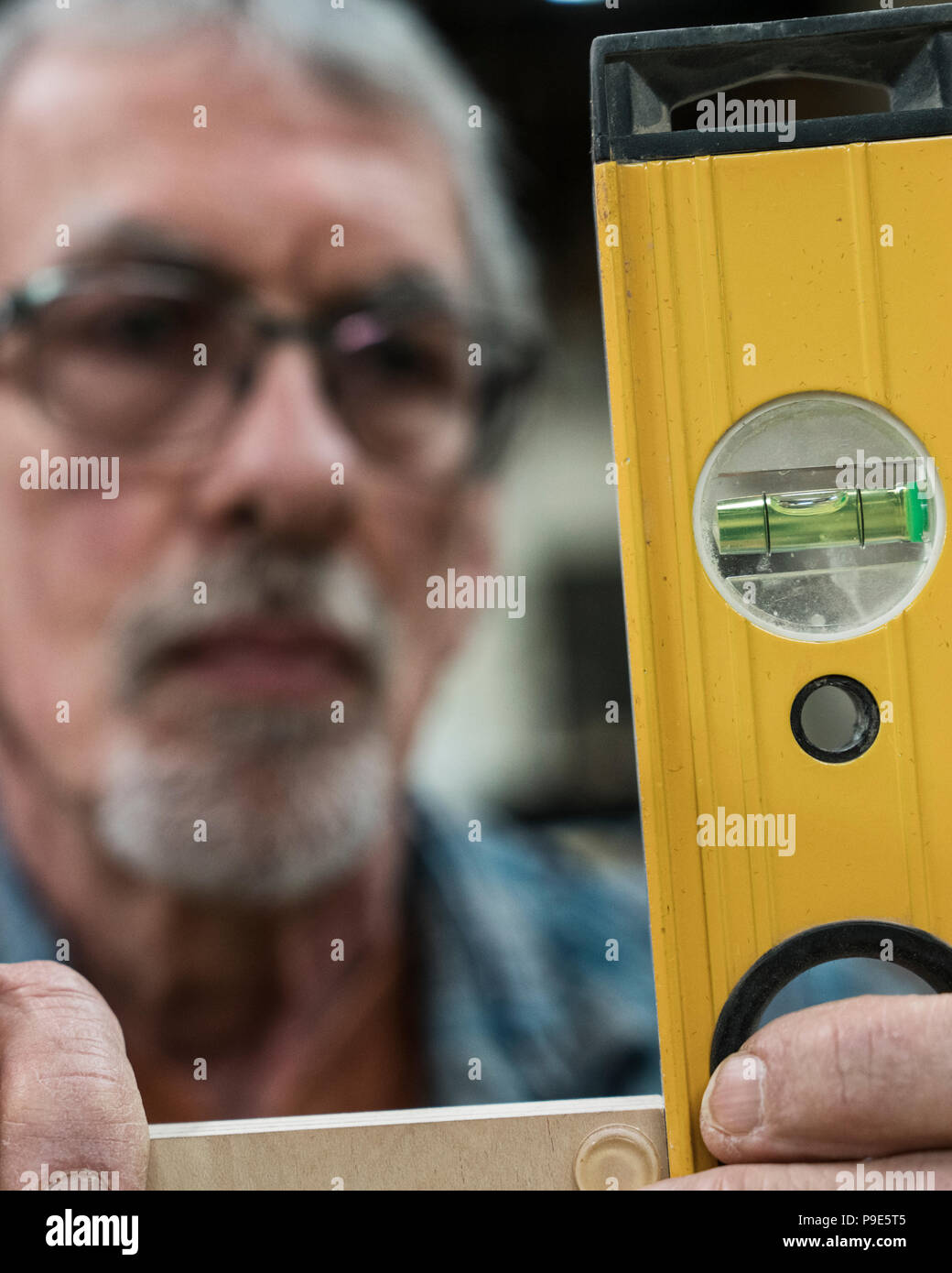 Ein älterer Mann mit Brille und Bart in einem holzarbeiter Shop, mit Hilfe einer Wasserwaage prüfen seine Arbeit. Stockfoto