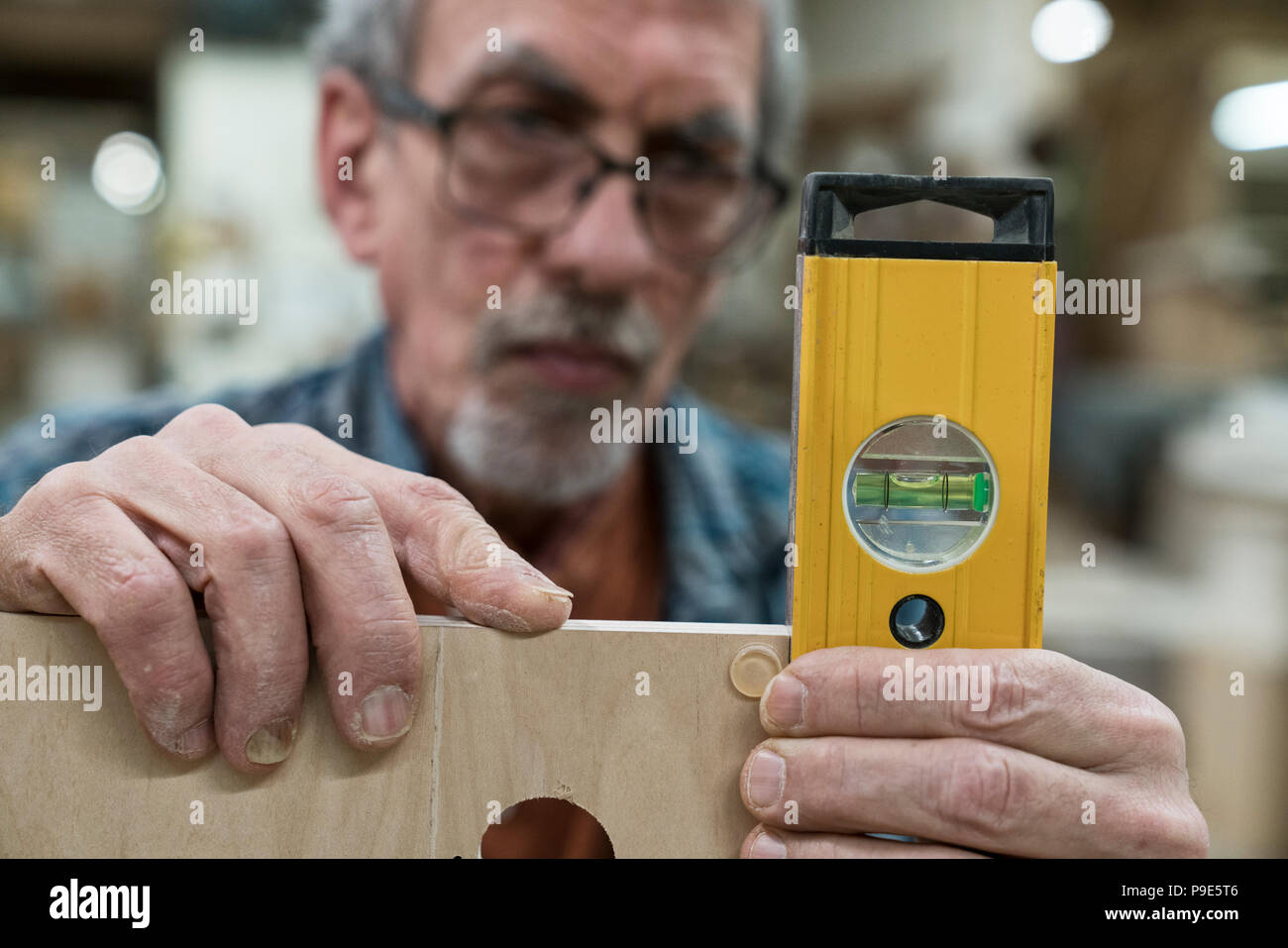 Ein älterer Mann mit Brille und Bart in einem holzarbeiter Shop, mit Hilfe einer Wasserwaage prüfen seine Arbeit. Stockfoto