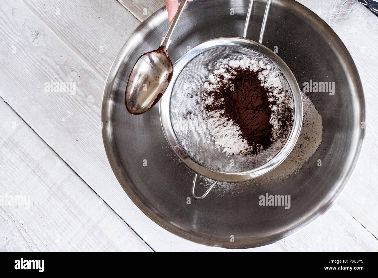 Eine Metallschale mit Zutaten und ein Sieb mit Kakaopulver. Stockfoto