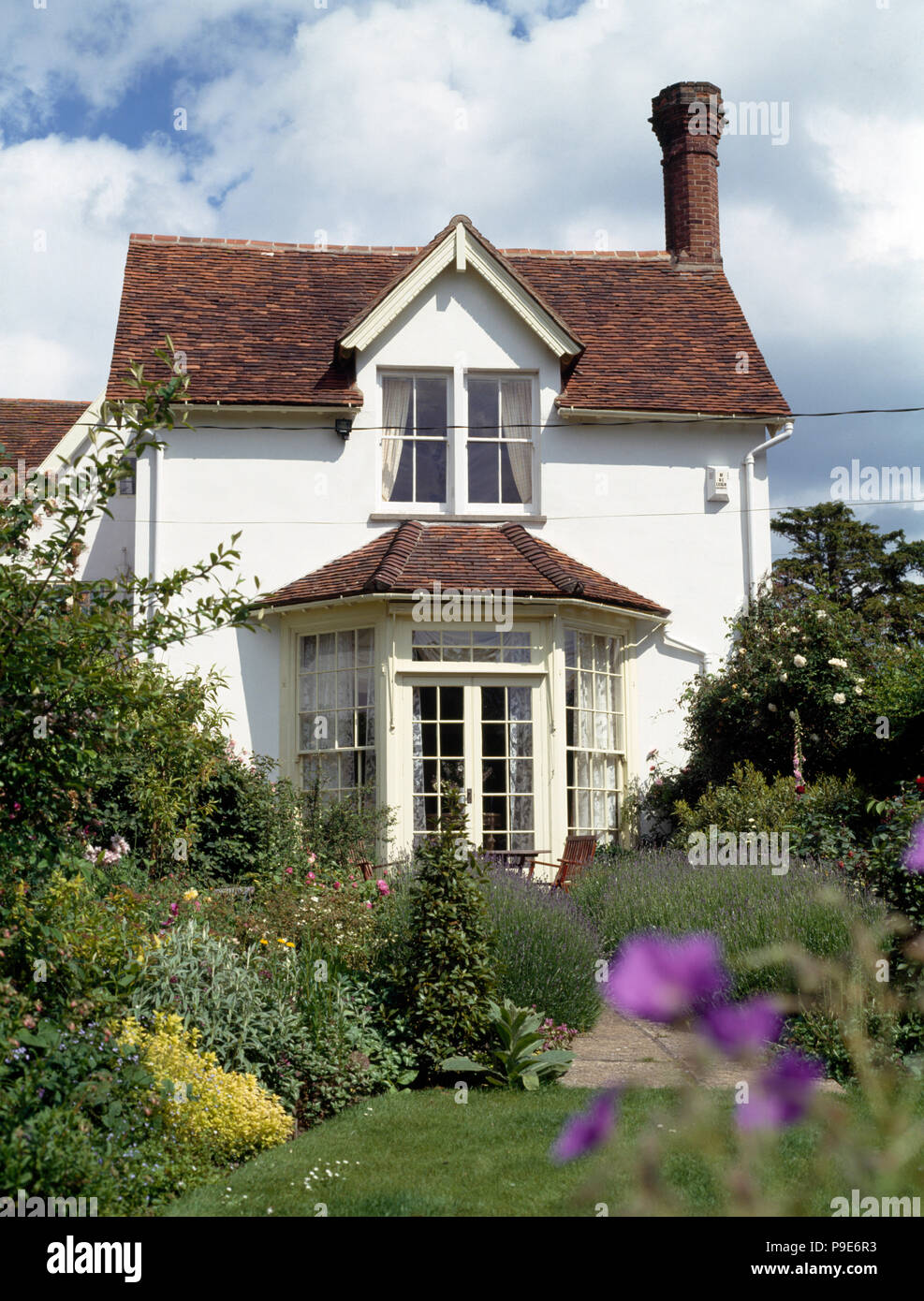 Äußere einer weiß lackierten Cottage mit französischen Fenstern in einer gut ausgestatteten Sommergarten Stockfoto