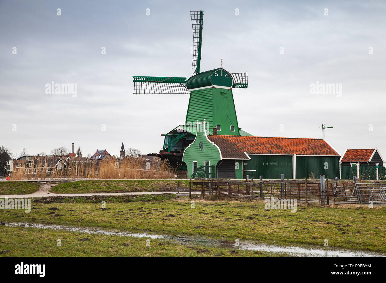 Alte Windmühle aus Holz in der Nähe von Green Scheunen am Fluss Zaan Küste, Zaanse Schans Stadt, beliebten touristischen Attraktionen der Niederlande. Vorort von Amsterdam Stockfoto