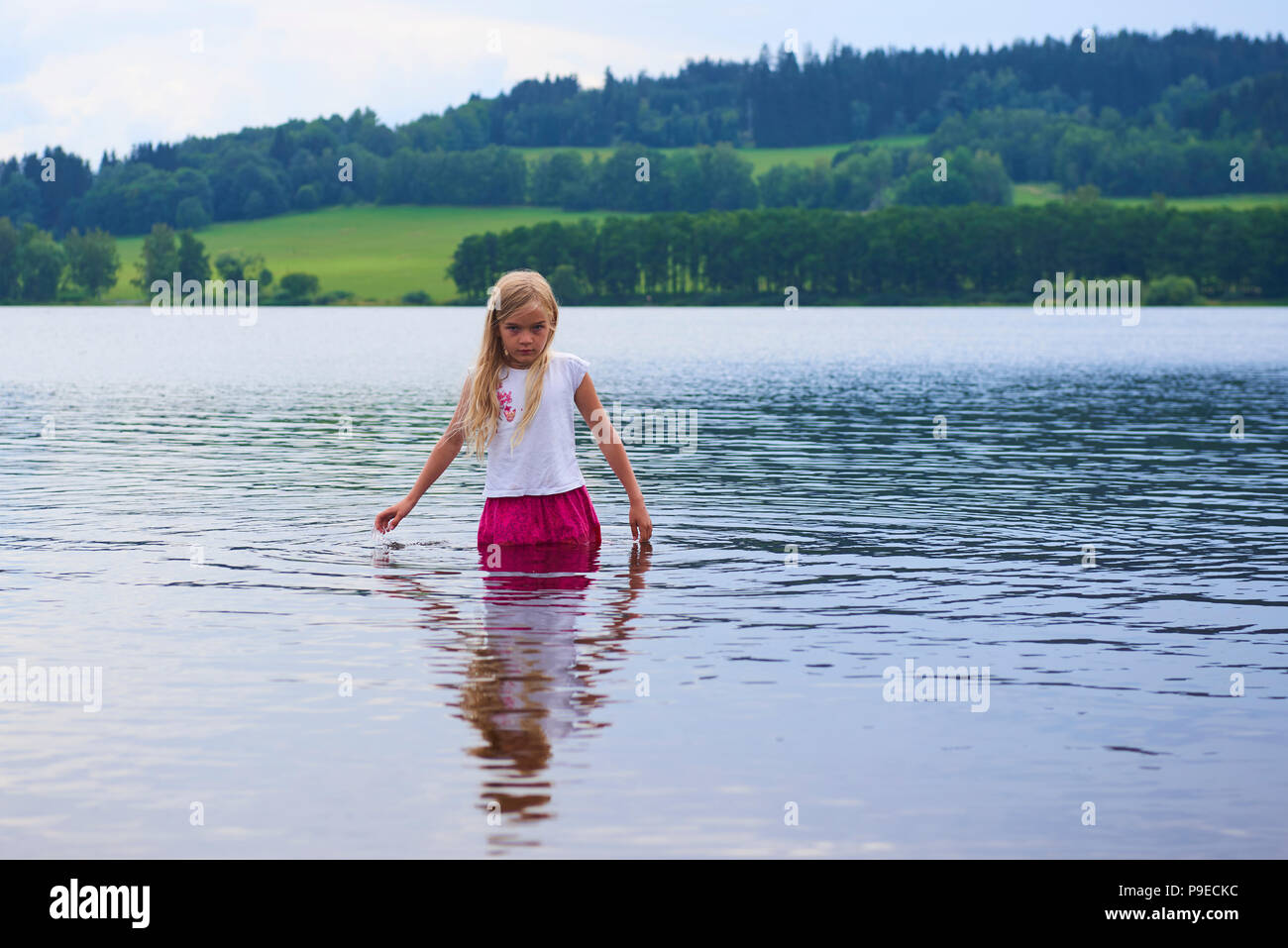 Kind traurig blondes Mädchen in Shirt und Rock stehen im Wasser angezogen Stockfoto