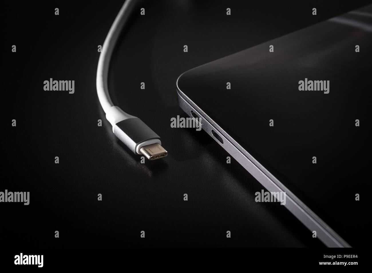 Anschließen des USB-Typ C Kabel zum Laptop auf schwarzem Hintergrund Stockfoto