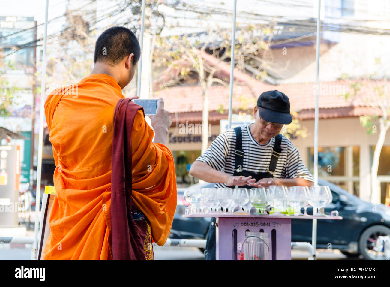 Buddhistischer Mönch Bilder aufnehmen als eine alte Thai Street Performer ist das Abspielen von Musik auf dem Wasser Gläser in Chiang Mai, Thailand Stockfoto