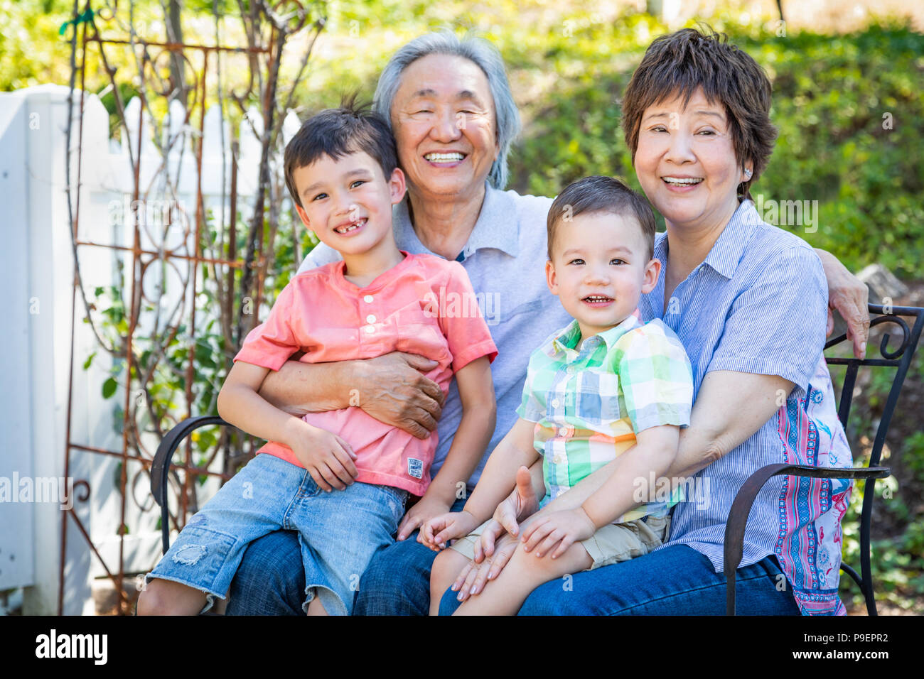 Chinesische Großeltern und gemischten Rennen Kinder sitzen auf der Bank Draußen Stockfoto