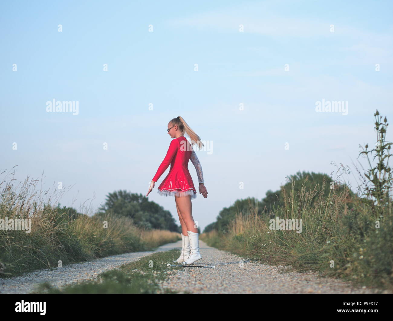 Bebrillter blonder Teen Majorette Mädchen Twirling Baton draußen im roten Kleid Stockfoto