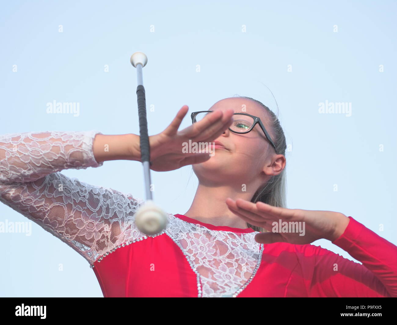 Bebrillter blonder Teen Majorette Mädchen Twirling Baton draußen im roten Kleid Stockfoto