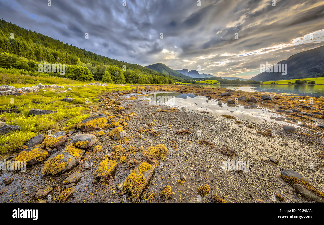 Fjord Landschaft mit Bergen im Hintergrund. Gezeitenzone mit Felsen und Steine bei Ebbe auf Eidsbygda Halbinsel Norwegen im HDR Stockfoto