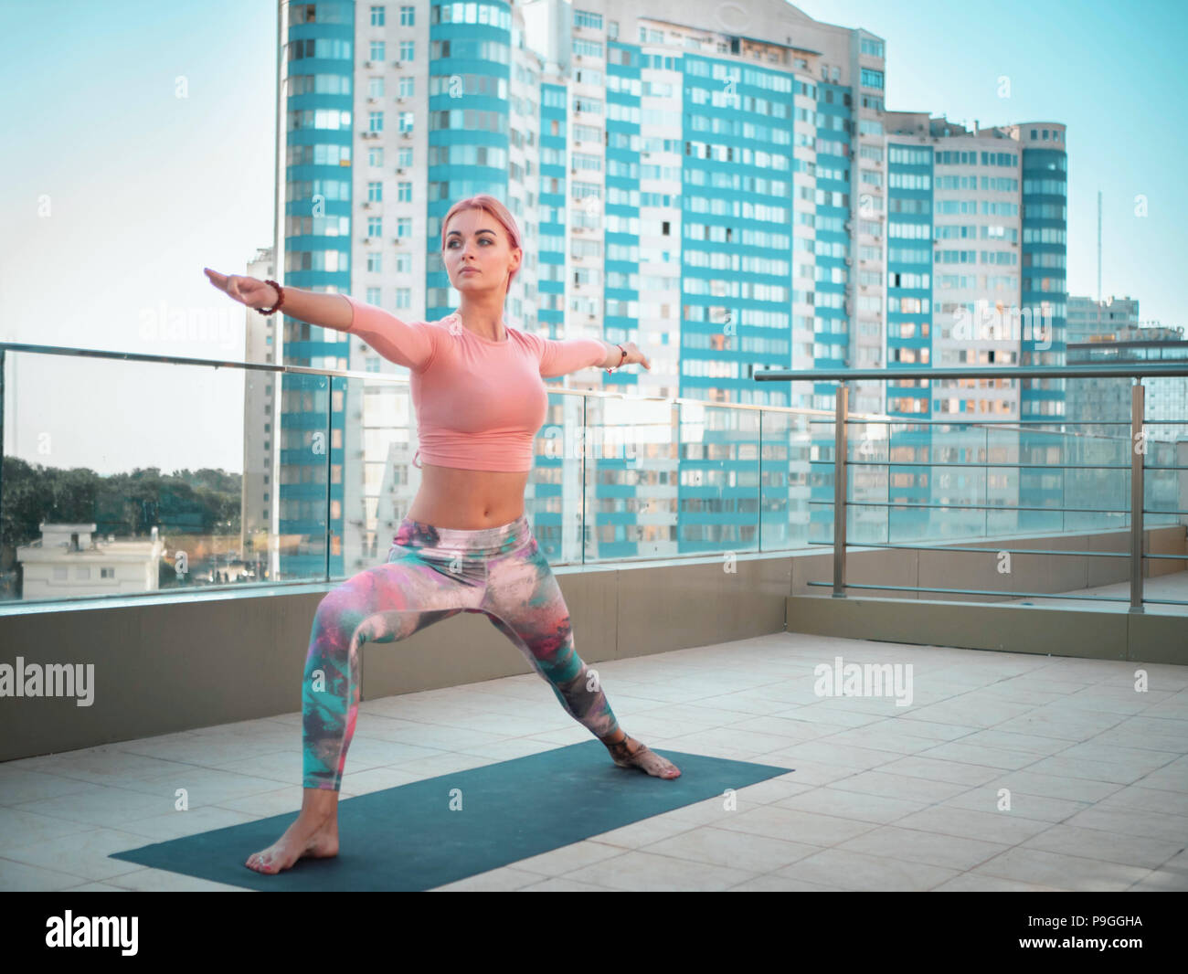 Junge schlanke Frau mit rosa gefärbten Haaren Yoga Praxis auf der Terrasse der modernen Stadt. Mädchen halten fit und gesund Körper entspannen Sie auf der Dachterrasse während der Praxis darstellen, Stockfoto