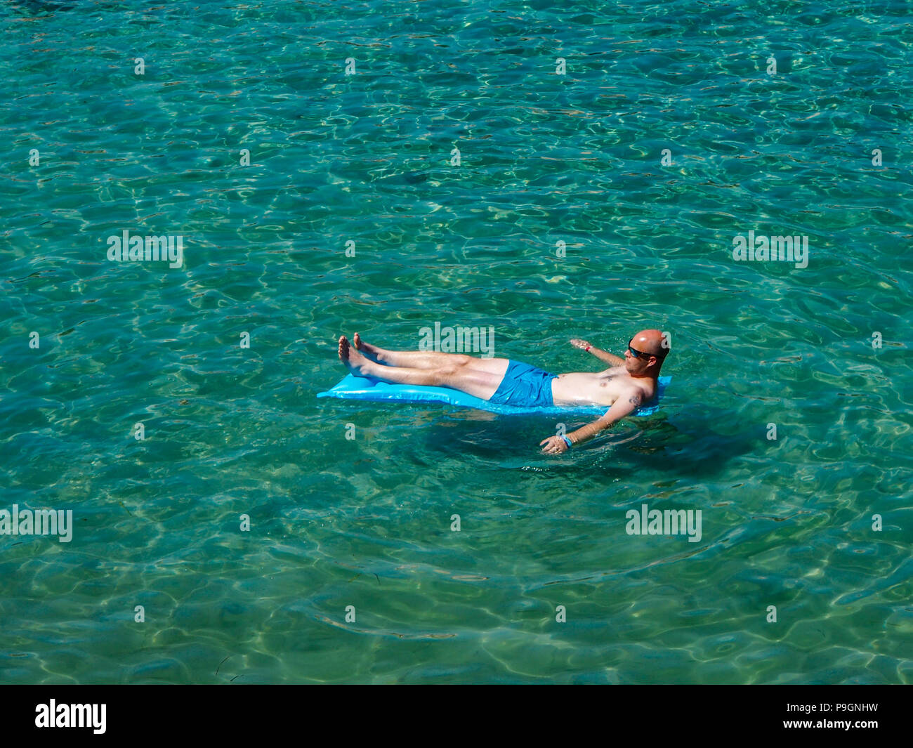 Ein Mann schwebt auf einem aufblasbaren in einem kristallklaren Meer Stockfoto