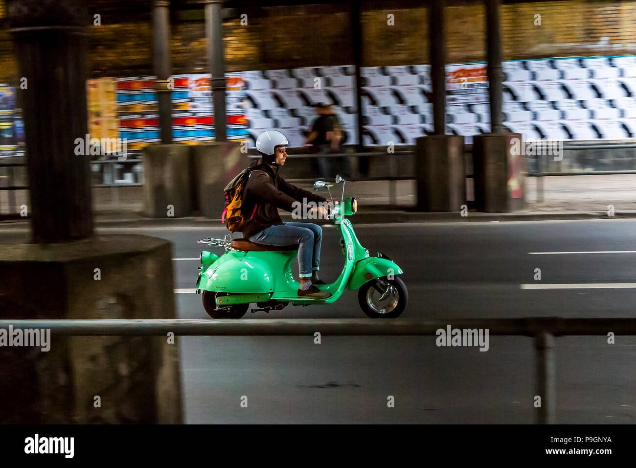 Ein Moped-Fahrer fährt seine Vespa in Berlin auf eine Straße unter einer Brücke. Stockfoto