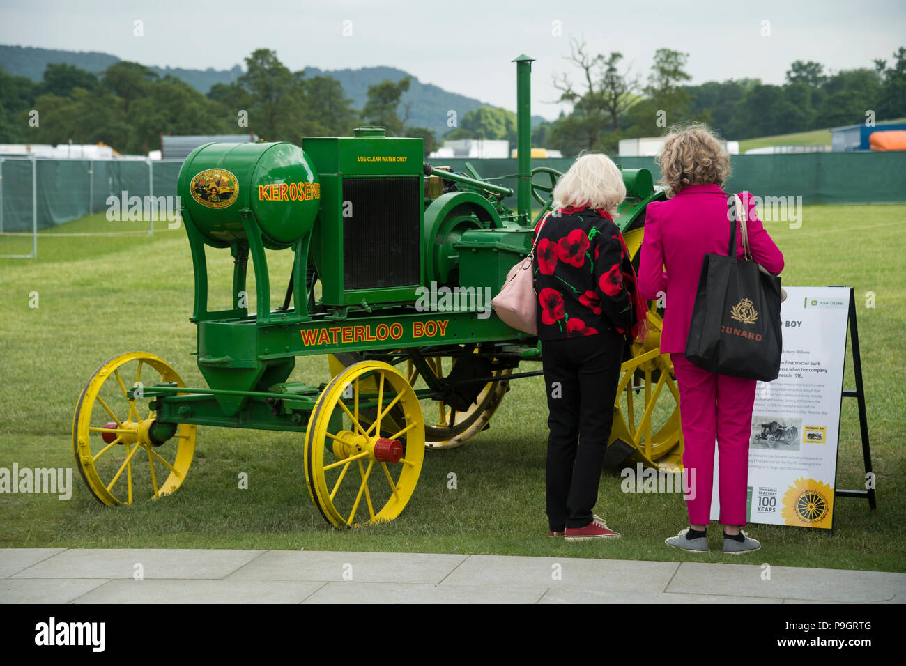 2 Frauen lesen Zeichen über & historisches Grün & gelb Kerosin Traktor (Waterloo Boy) an der RHS Chatsworth Flower Show, Derbyshire, England, UK geparkt. Stockfoto