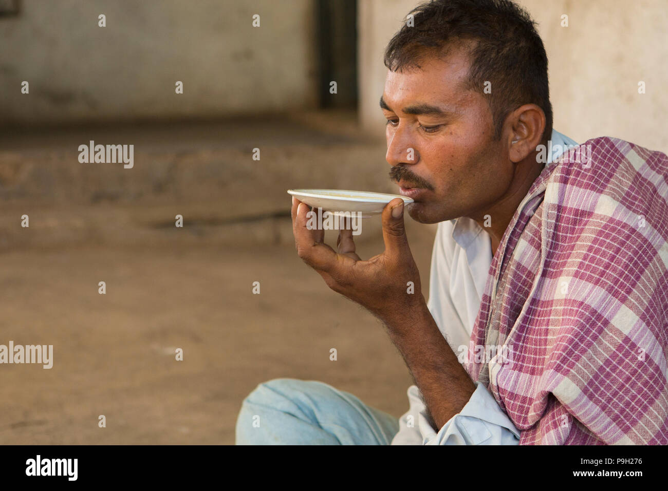 Ein Landwirt trinken Chai aus einer Untertasse an ihrem Haus in Ahmedabad, Indien. Stockfoto