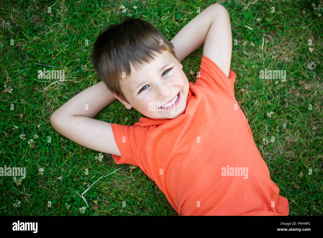 Niedliche Happy 6 Jahre alter Junge liegend auf grünem Gras und lächelnd. Stockfoto