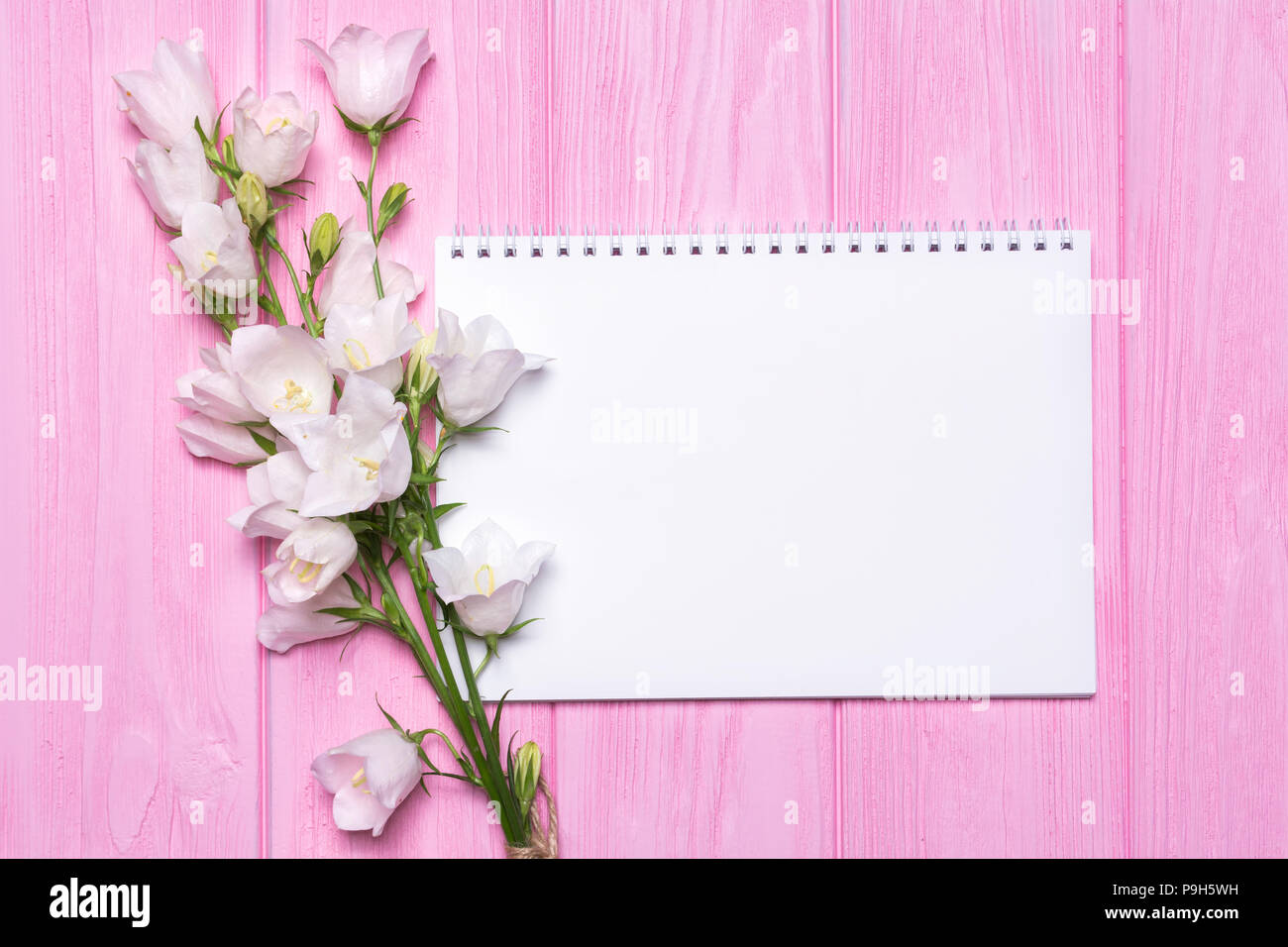 Weiße Blumen Glocken und ein leeres Notebook für Ihr Text auf einem rosa Hintergrund aus Holz. Stockfoto