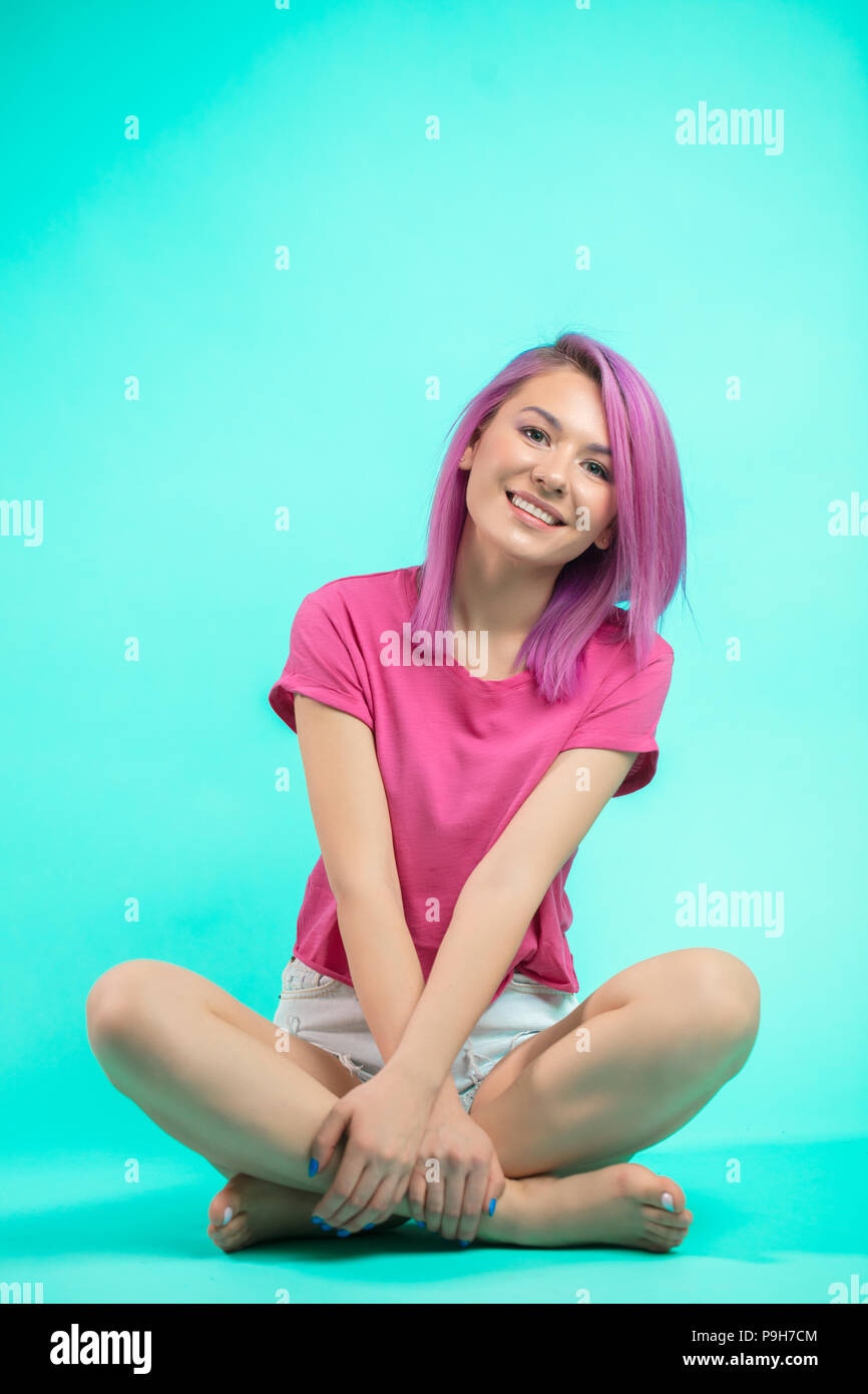 Schüler Mädchen sitzen mit gekreuzten Barfuß leggs am Studio blauen Boden an der Kamera schaut. Stockfoto