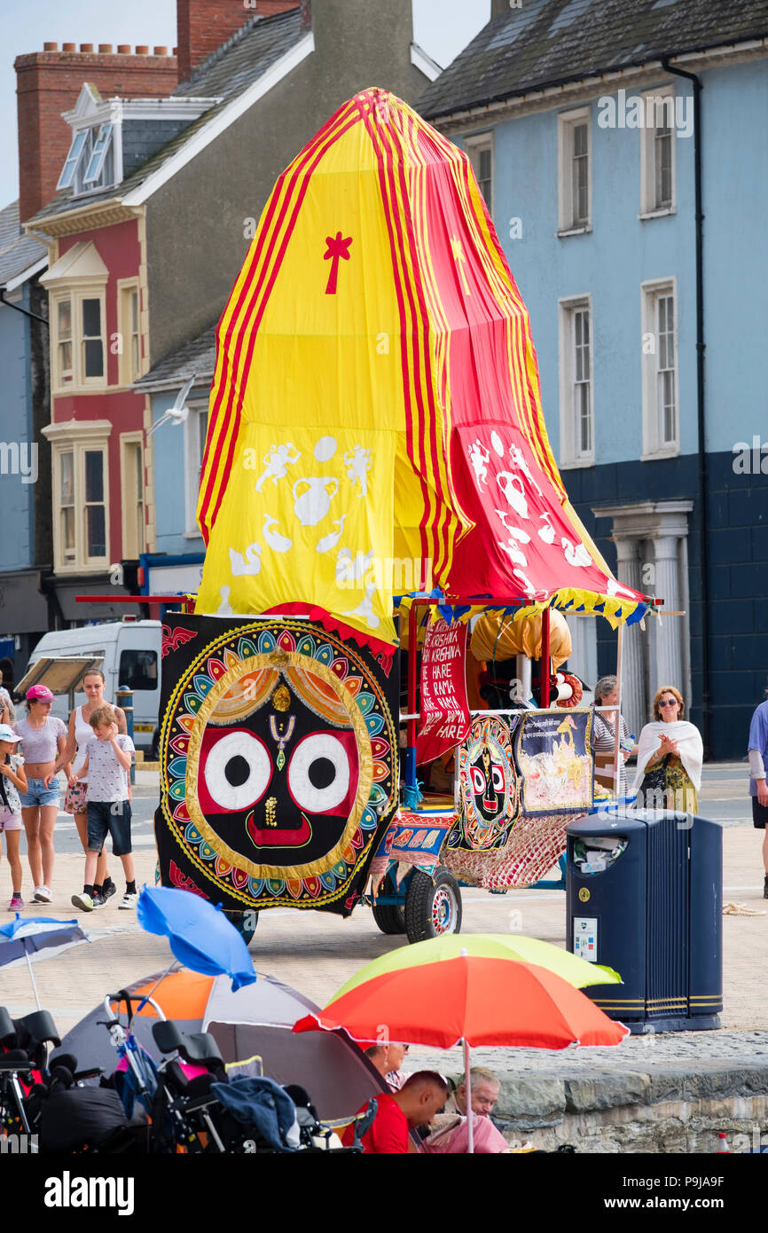 Glaube und Religion auf dem UK: Eine Gruppe von Hare Krishna Devotees mit ihrer "Ratha' eine bunte votive mobile Tempel Wagen der Gottheit Herr Jagannath, Chanting, wie Sie schleppen es entlang der Promenade in Aberystwyth, Wales UK, an einem Sommernachmittag Stockfoto