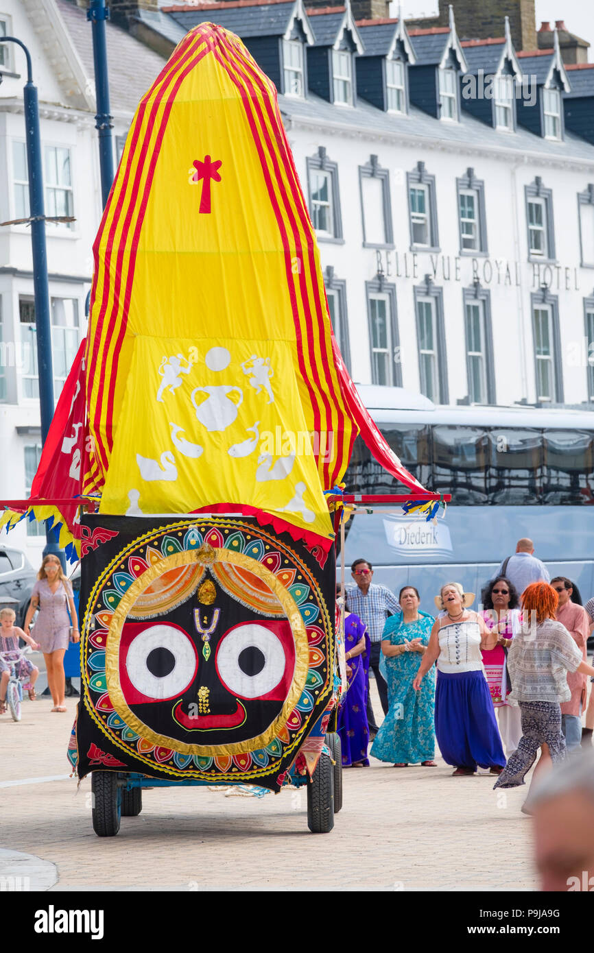 Glaube und Religion auf dem UK: Eine Gruppe von Hare Krishna Devotees mit ihrer "Ratha' eine bunte votive mobile Tempel Wagen der Gottheit Herr Jagannath, Chanting, wie Sie schleppen es entlang der Promenade in Aberystwyth, Wales UK, an einem Sommernachmittag Stockfoto
