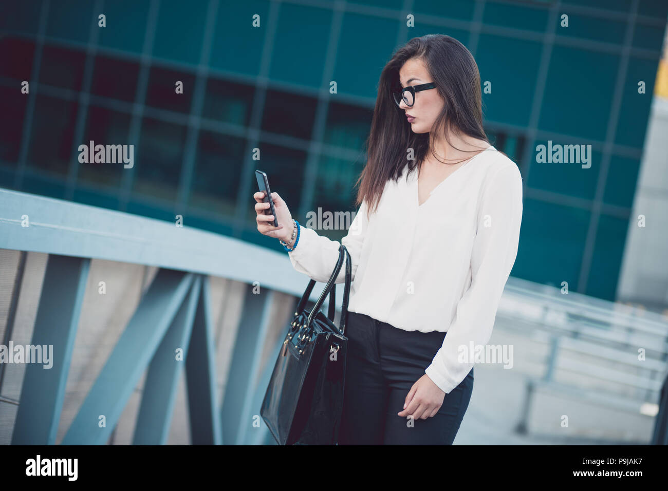 Schöne brünette Frau mit weißem Hemd von SMS-Nachrichten auf dem Smartphone zu Fuß auf der Straße in einem bewölkten Tag. Stockfoto