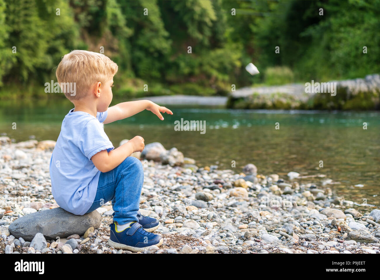 Kind allein mit blonden Haaren, wirft einen Stein am Ufer des Flusses, sonnigen Tag, horizontale Foto Stockfoto