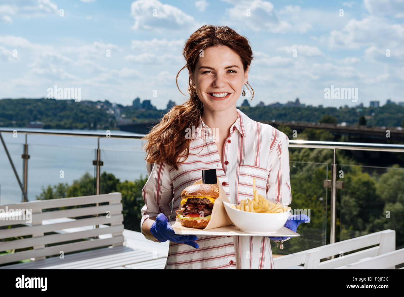 Lächelnde Frau mit Pferdeschwanz essen Kartoffeln und Fleisch Burger Stockfoto