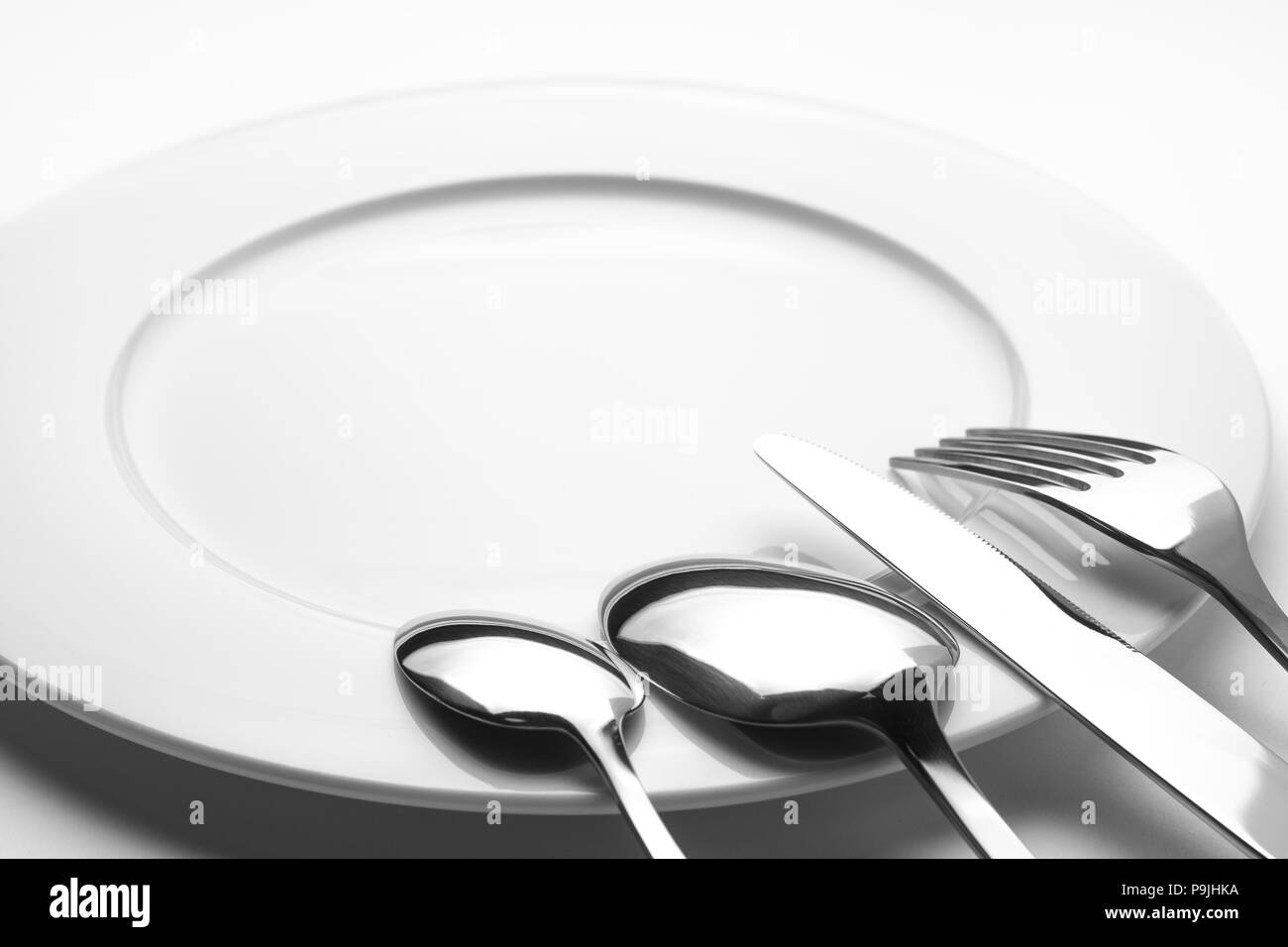 Löffel, Löffel, Gabel und Messer auf einem leeren Teller, Besteck und Kopieren, auf weißem Hintergrund Stockfoto