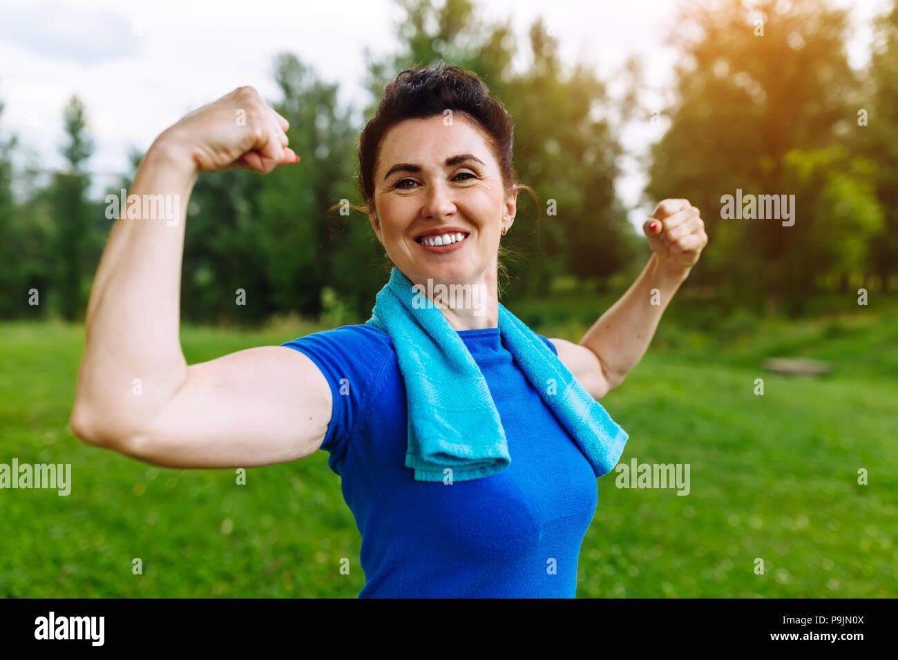Lächelnd Senior Frau flexing Muskeln Outdoor im Park. Ältere Frauen zeigen Bizeps. Gesunden Lebensstil Konzept. Copyspace. Stockfoto