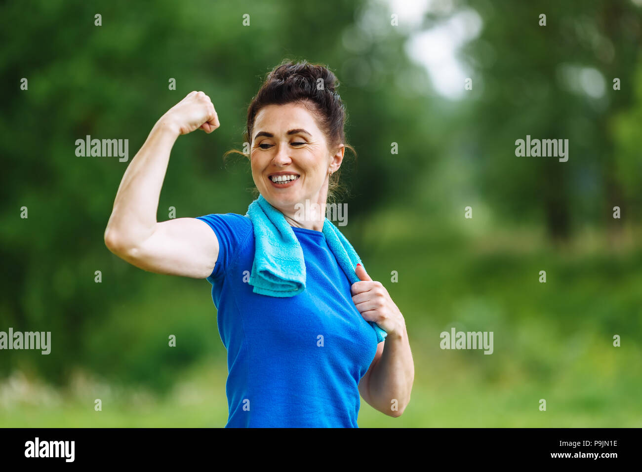 Lächelnd Senior Frau flexing Muskeln Outdoor im Park. Ältere Frauen zeigen Bizeps. Gesunden Lebensstil Konzept. Copyspace. Stockfoto