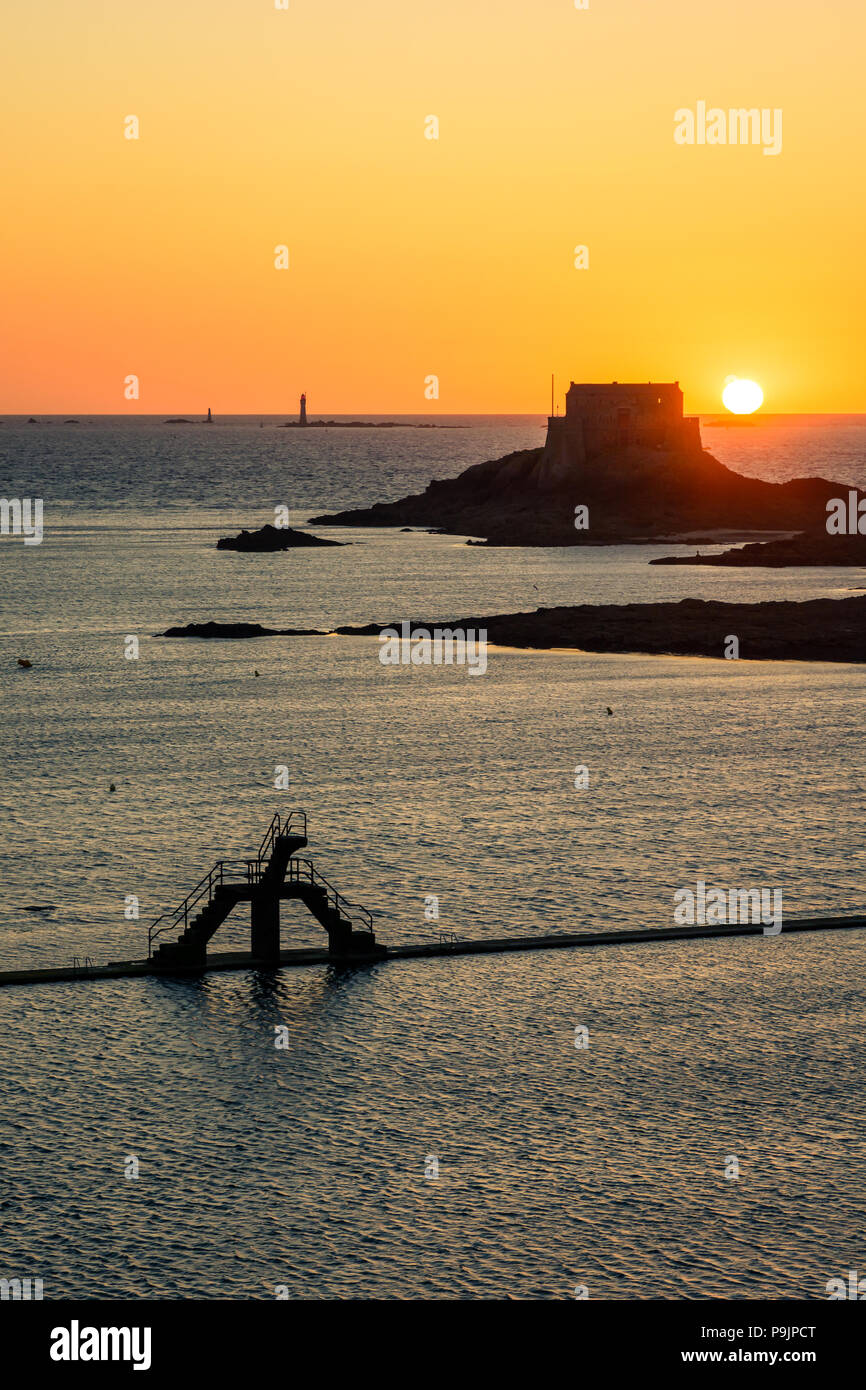 Die Sonne hinter den Petit Insel, vor der Stadt Saint-Malo mit dem sewater Pool von Bon Secours Strand und seine Sprungturm. Stockfoto
