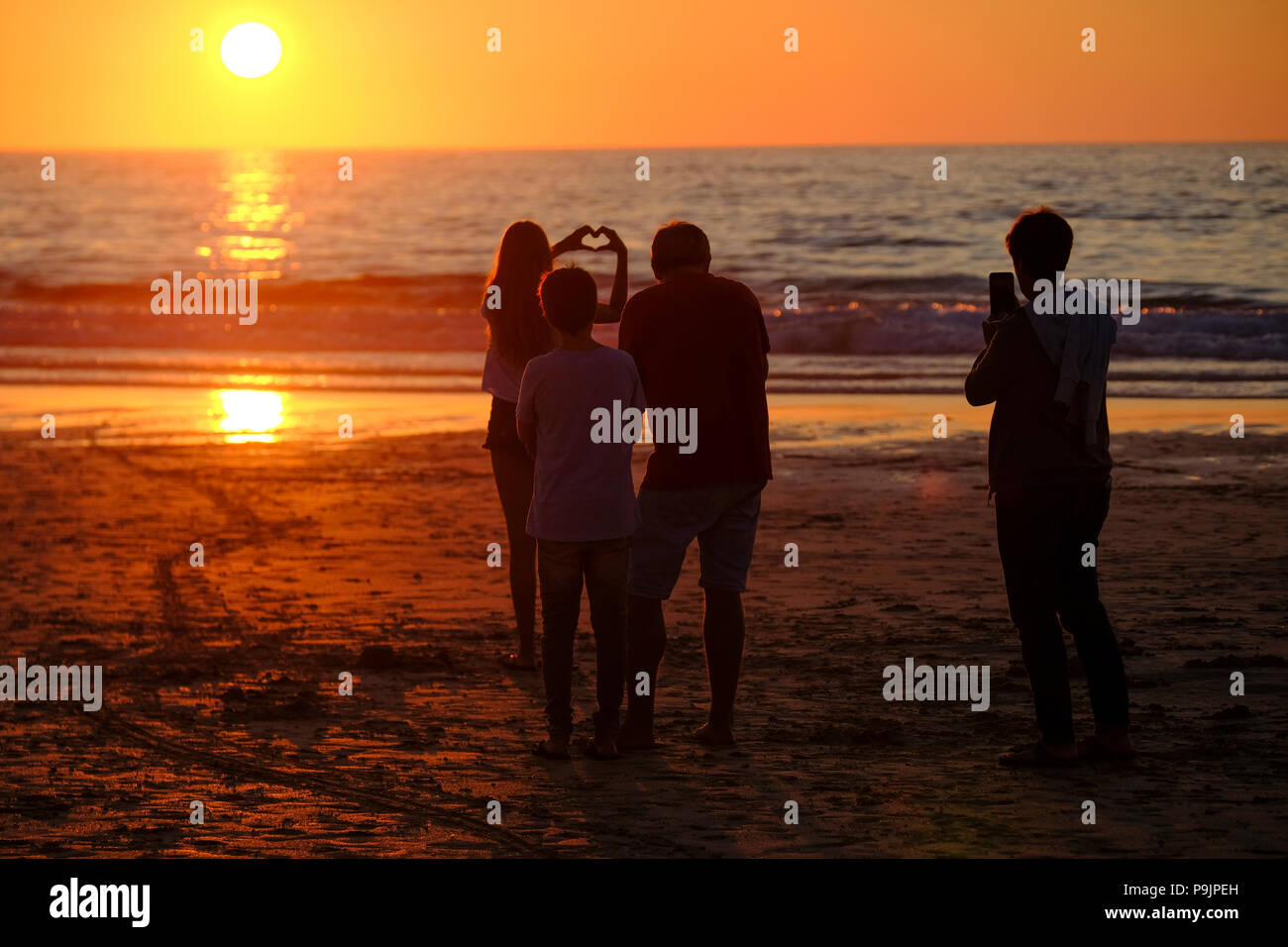 Junge Frauen, die Form eines Herzens mit ihren Händen wie die Sonne auf Portmeor Strand in St Ives, Cornwall setzt Stockfoto