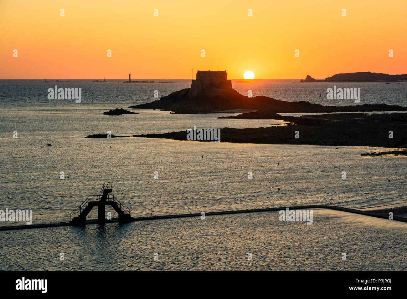 Die Sonne hinter den Petit Insel, vor der Stadt Saint-Malo mit dem sewater Pool von Bon Secours Strand und seine Sprungturm. Stockfoto