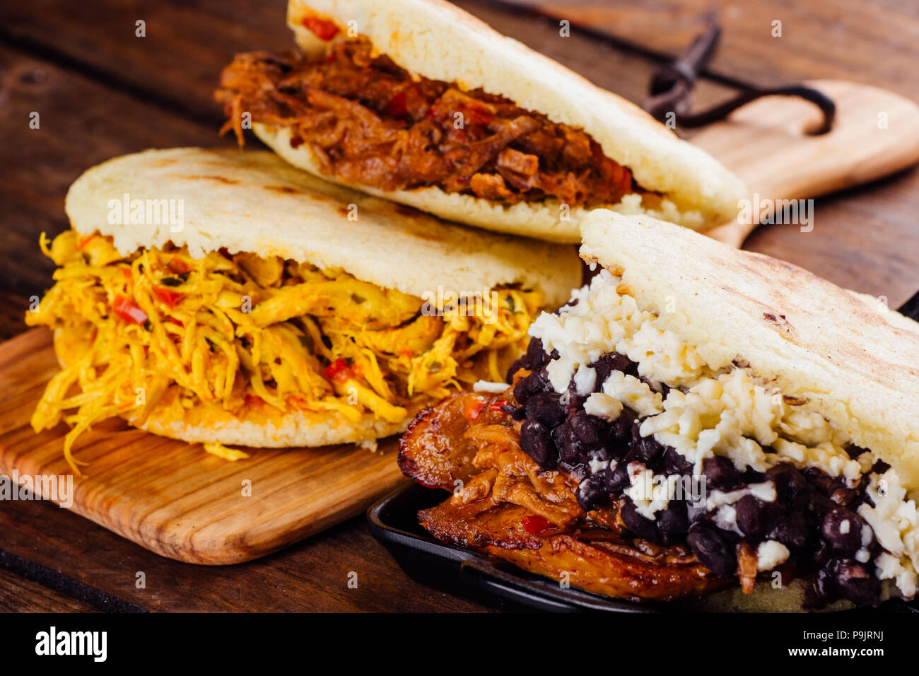 Venezolanische traditionelle Arepas frisch gemacht, mit 3 verschiedenen Füllungen Huhn Geschmack, gebratenes Fleisch und pabellon auf einer hölzernen Hintergrund Stockfoto