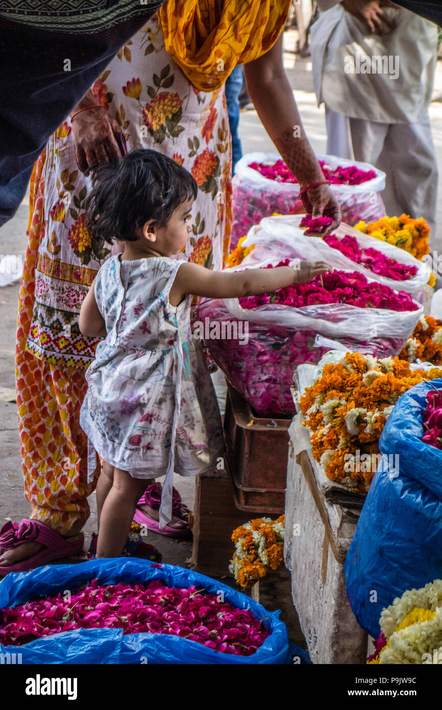 Süße kleine indische Mädchen mit einer Frau mit Blumen in einem Stall in Alt Delhi, Indien Stockfoto