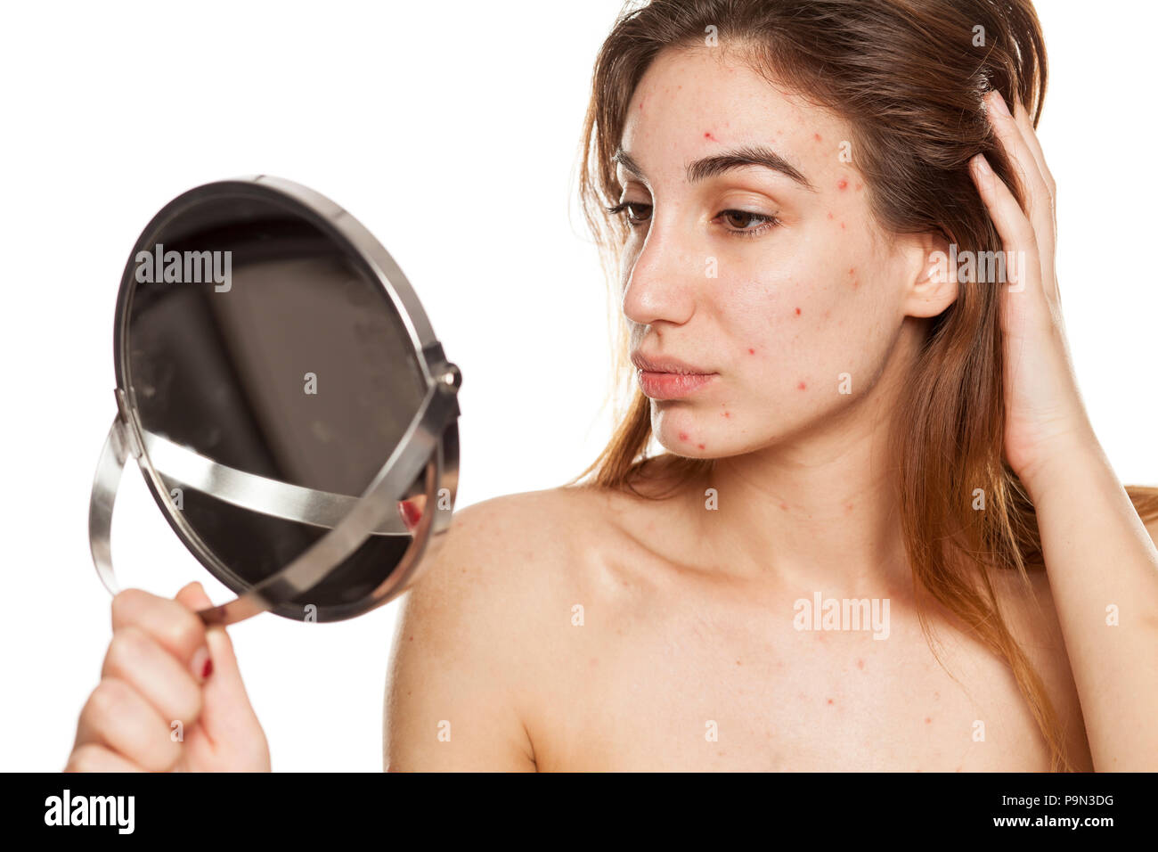 Junge Frau mit problematischer Haut und ohne Make-up ihr Blick in den Spiegel auf weißem Hintergrund Stockfoto
