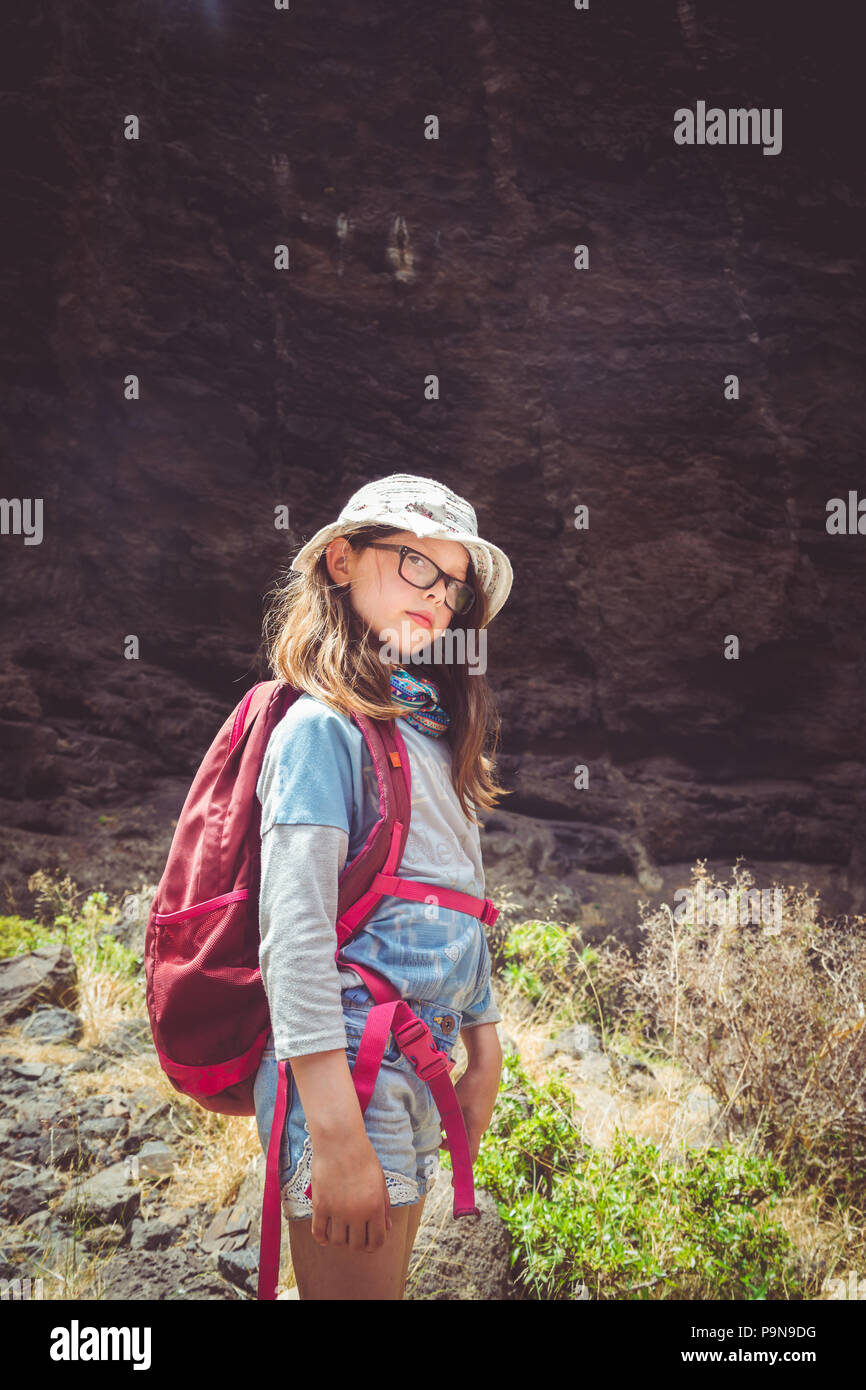 Eine kaukasische Mädchen Pausen während einer Wanderung an einem heißen Tag gegen eine felsige Bergkulisse trägt einen Rucksack, Mütze, Shorts und Gläser Masca, Teneriffa Stockfoto