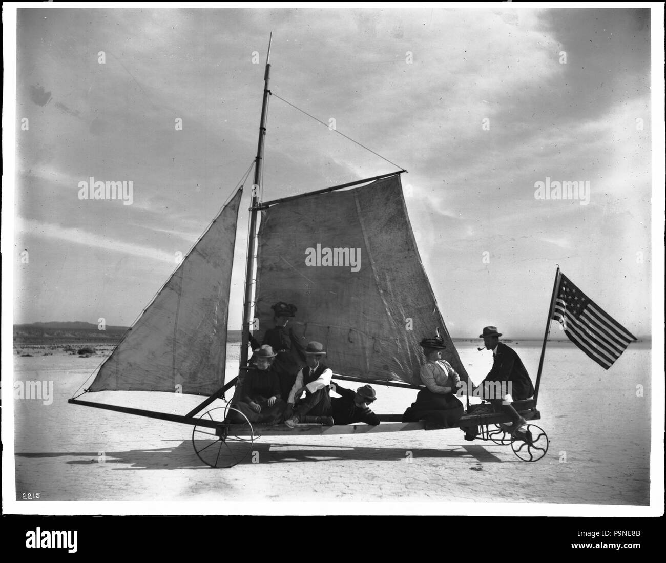 . Englisch: "The Desert Queen' Segeln auf der Mojave Wüste, 1905 Foto von der "Desert Queen' Segeln auf Rosamond trockenen See in der Antelope Valley der westlichen Mojave Wüste im Jahre 1905. Die Desert Queen wurde gebaut und verwendet von Bergleuten, drei Meilen von der trockenen See zu überqueren. Die segeln Fahrzeug mit vier Rädern, Segel (Spinnaker & großsegel) und eine Fahne. Fünf Passagiere (drei Frauen, zwei Männer) sitzen auf dem flachen Skelett Plattform, während ein Mann, Rauchen ein Rohr, das Lenkrad betätigt. Das Schiff ist auf der linken Seite leitete. Rufnummer: CHS-2215 Fotograf: Pierce, C.C. (Charles C.), 1861-1946 Filena Stockfoto