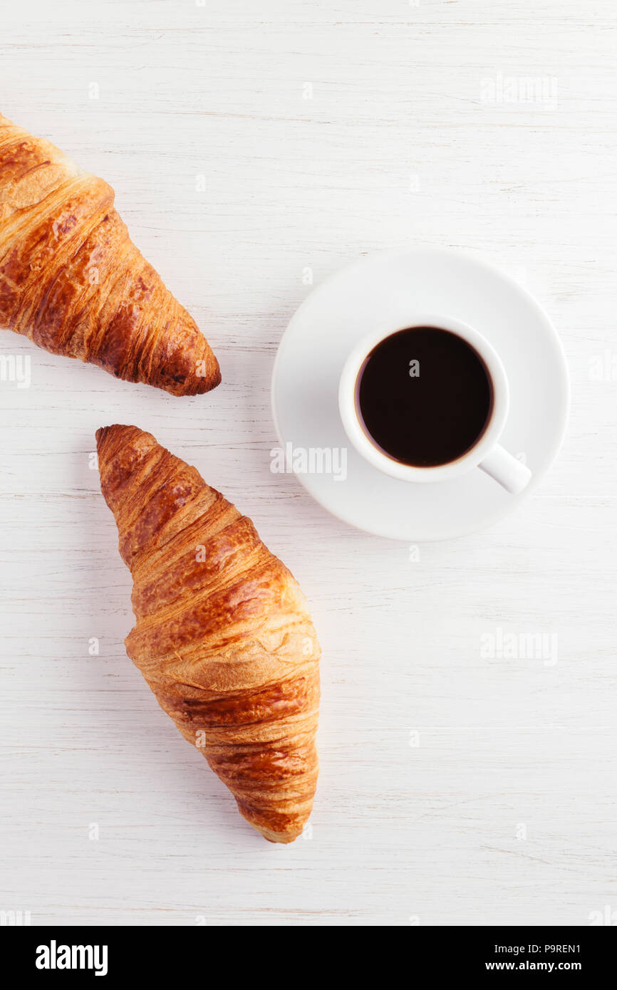 Eine Tasse Kaffee und zwei Croissants auf weiße Holztisch. Traditionelles französisches Frühstück. Ansicht von oben. Stockfoto