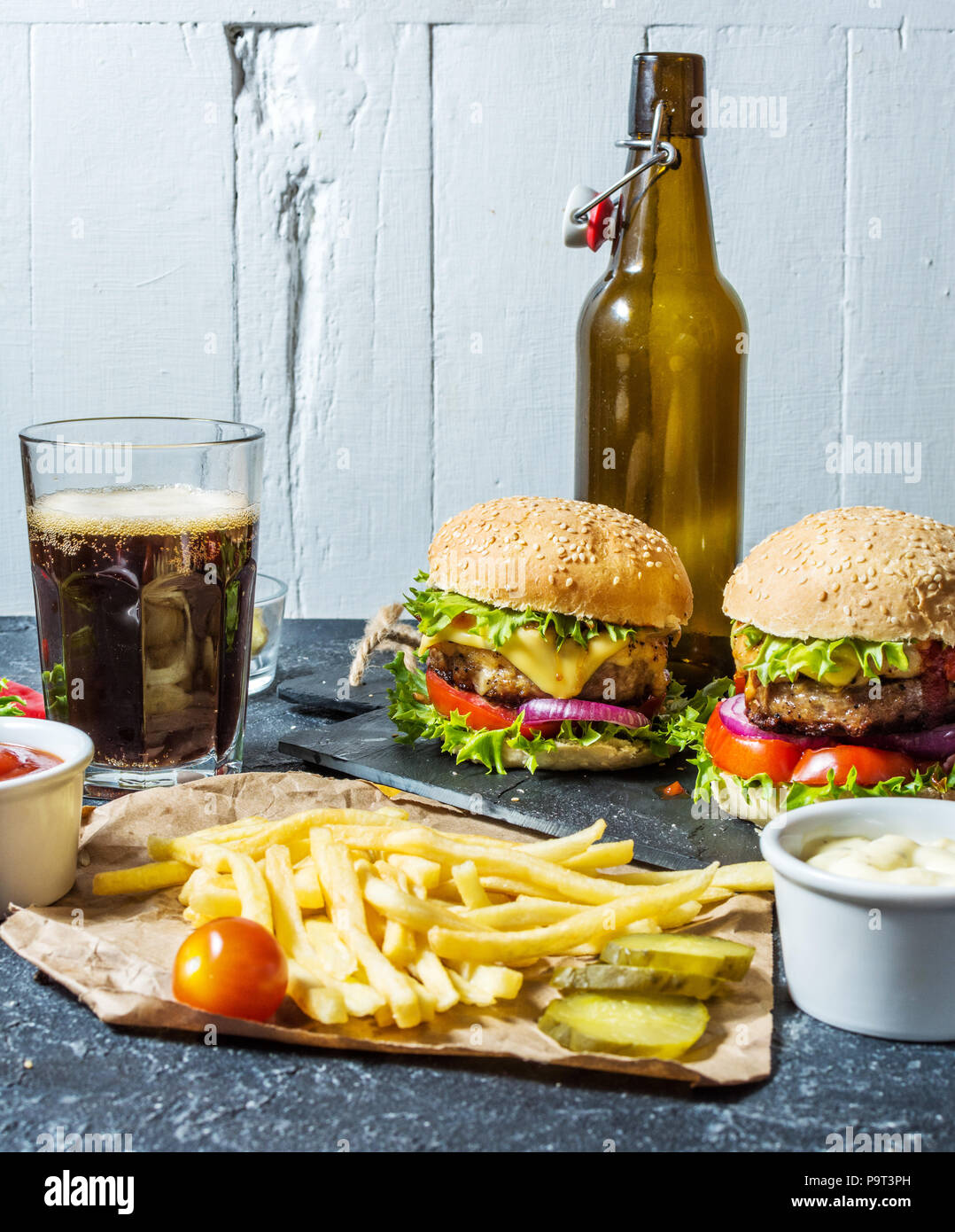 Hausgemachte Burger mit Rindfleisch und mit Bratkartoffeln und Glas kalten dunklen Bier auf Tisch aus Stein. Stockfoto