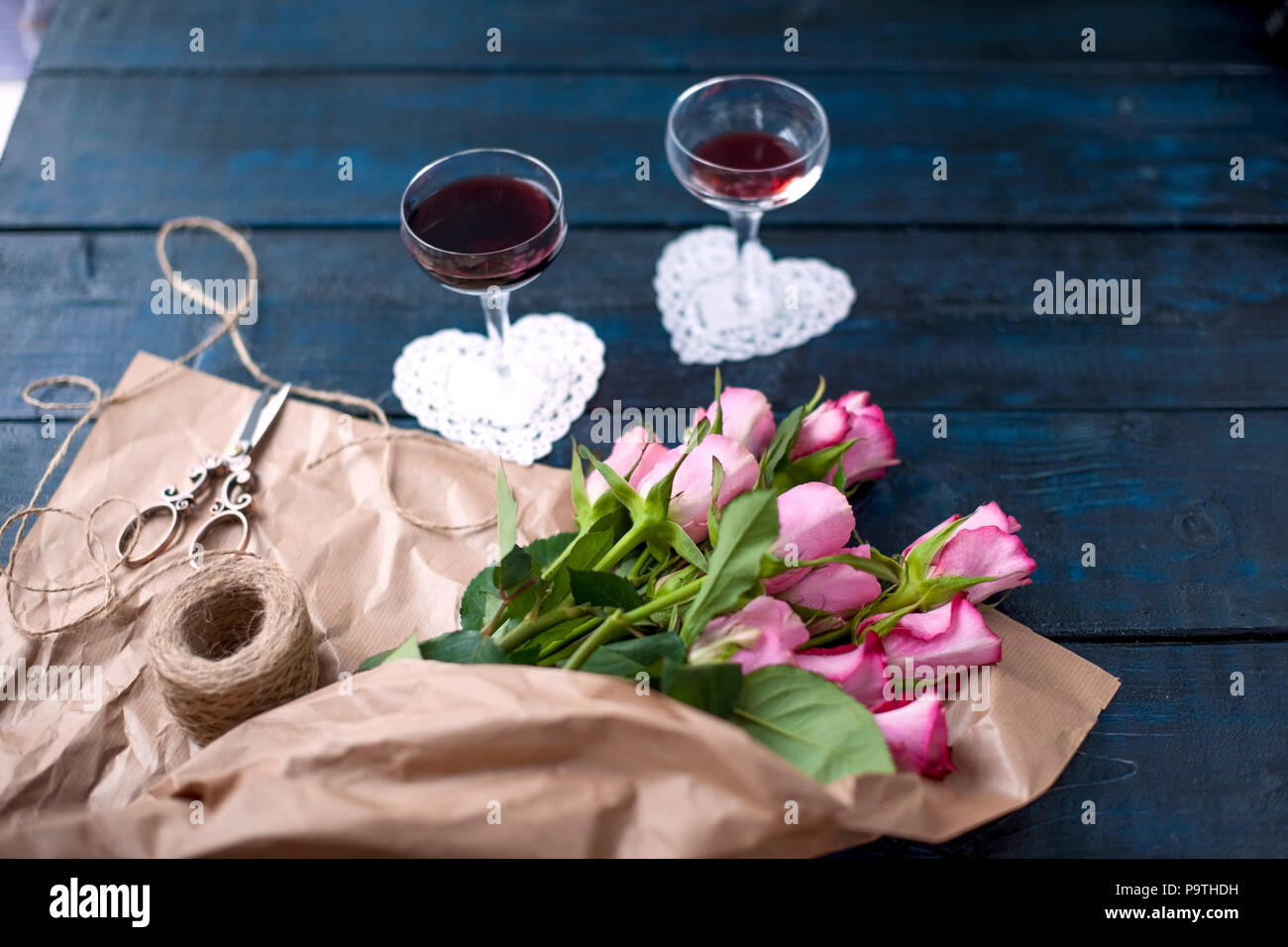 Zwei Gläser Rotwein in einen dunklen Tisch, ein Blumenstrauß aus Rosen in braunem Papier. Zwei weiße Herzen und makkaroni Kekse. Freier Platz für Text oder Postkarten. Stockfoto