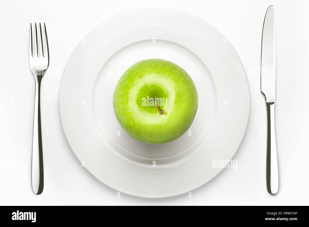 Diät Konzept, grüner Apfel auf einem weissen Teller, Gabel, Messer, Gewicht Stockfoto
