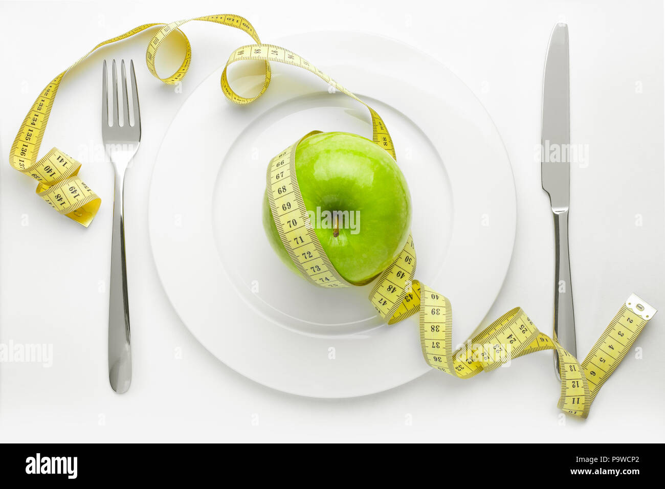 Diät Konzept, grüner Apfel auf einem weissen Teller, gelb Messabgriff Stockfoto