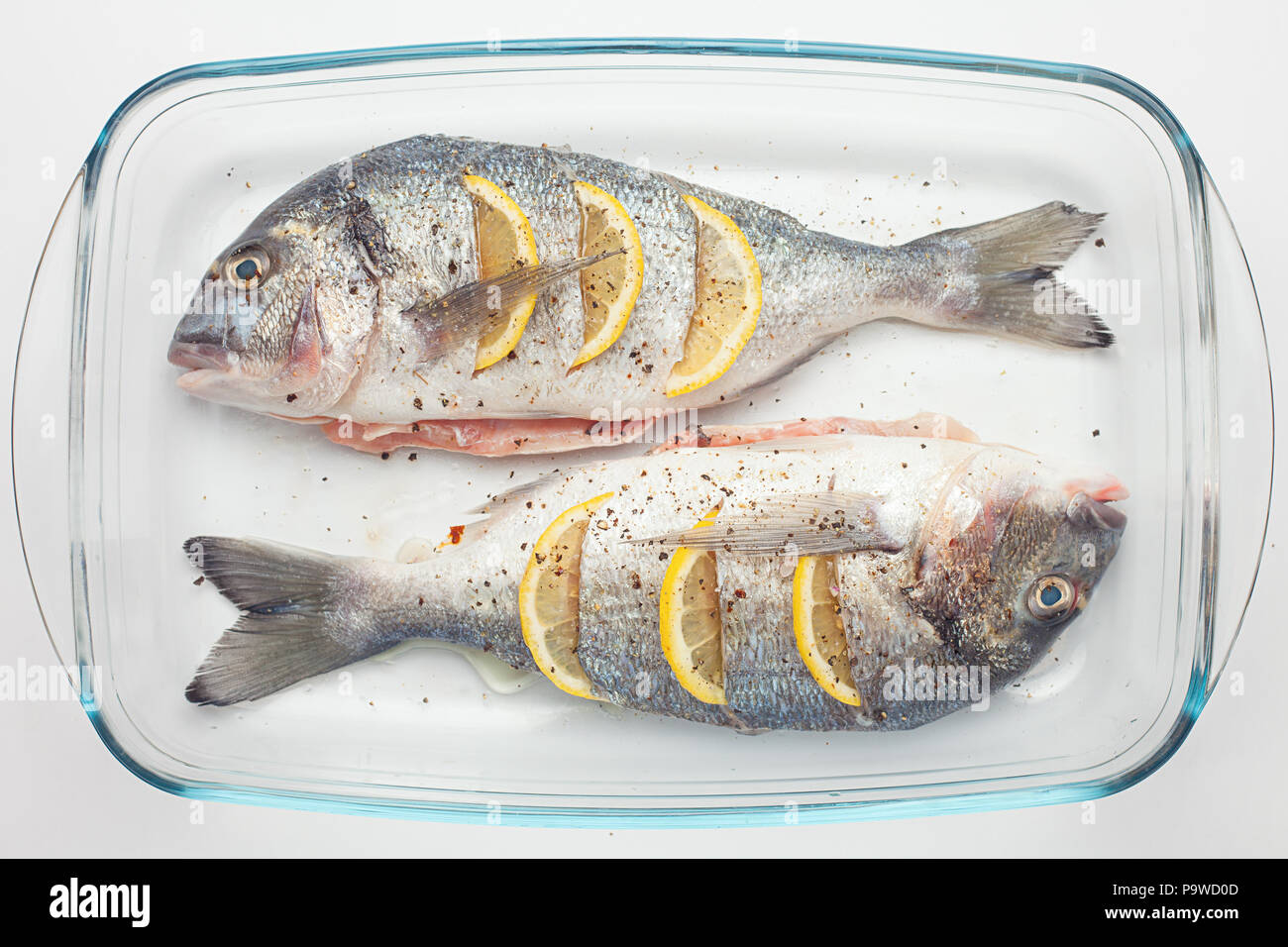 Raw dorado roher Fisch mit Zitrone und Gemüse, Tomaten, Zwiebeln, Gewürze auf einem Glas pan Stockfoto