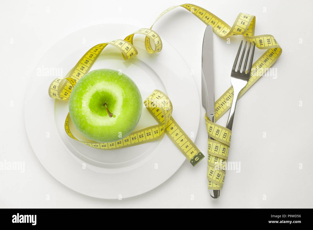 Diät Konzept, grüner Apfel auf einem weissen Teller, gelb Messabgriff Stockfoto