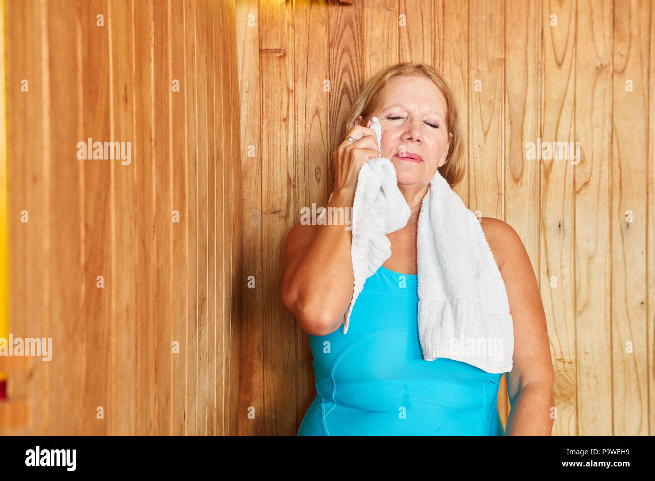 Ältere Frau schwitzt in der Dampfsauna und wischt sich den Schweiß von Stockfoto
