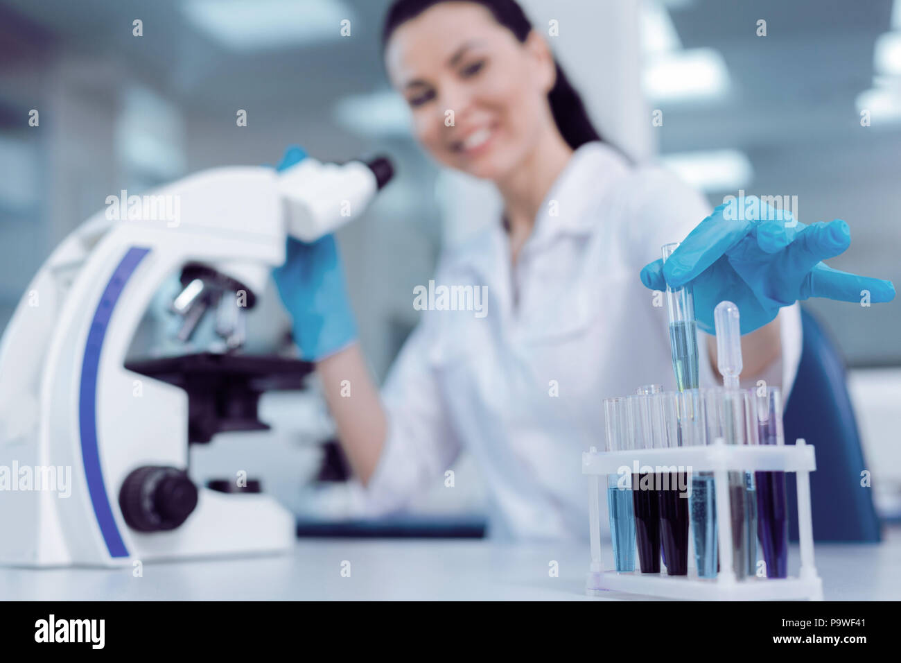 Professionelle Studien. Fröhliche positive freudige Wissenschaftler lächelnd und unter einem Reagenzglas aus dem Rack heraus, während Sie die biologische Studien Stockfoto