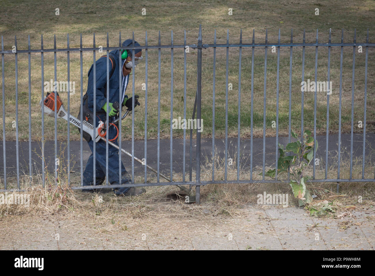 Der Auftragnehmer verwendet eine strimmer auf Unkraut entlang der Geländer von Ruskin Park, am 5. Juli 2018 in London, England. Stockfoto