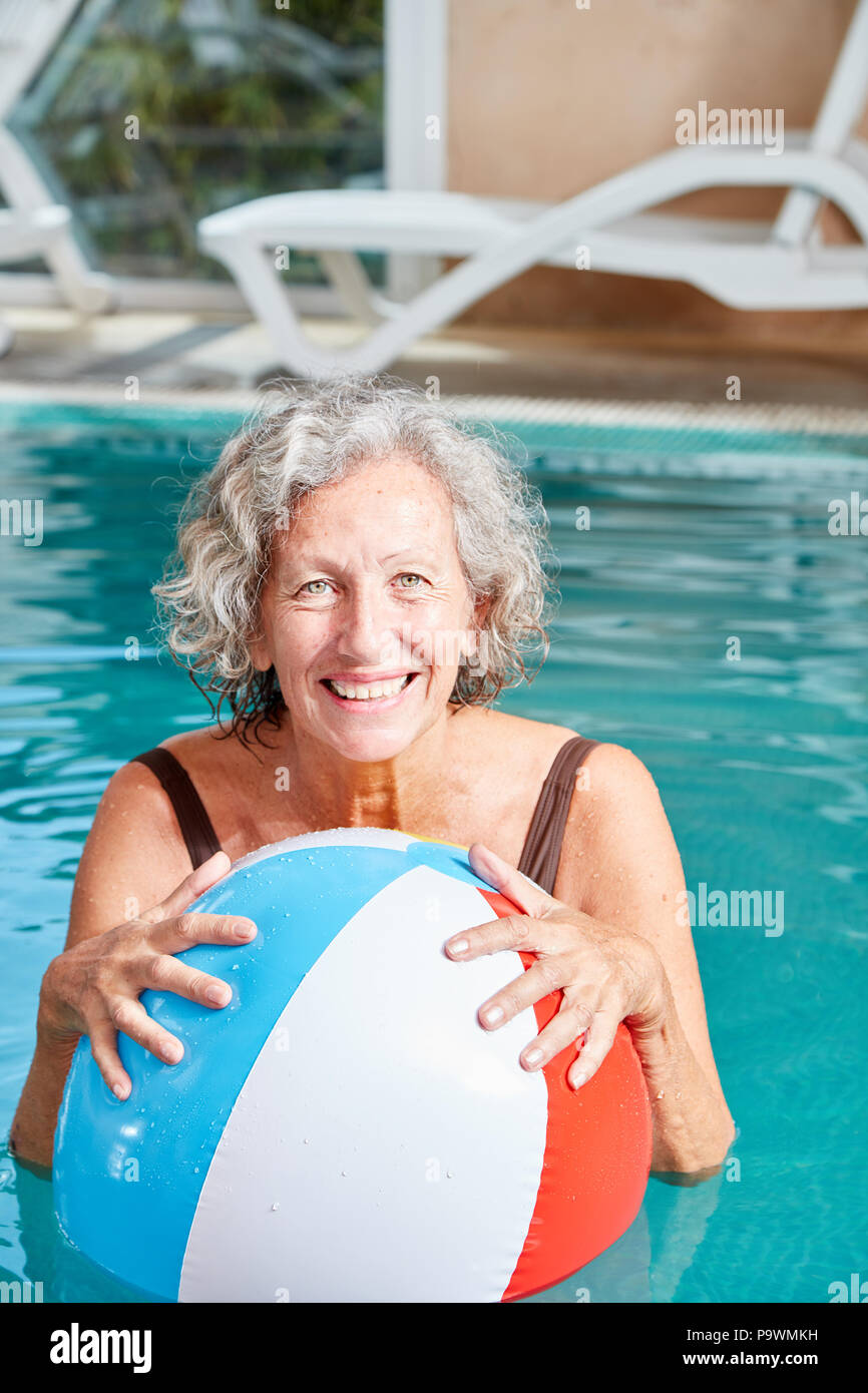 Vitale ältere Frau mit einem bunten Ball in den Pool im Urlaub Stockfoto