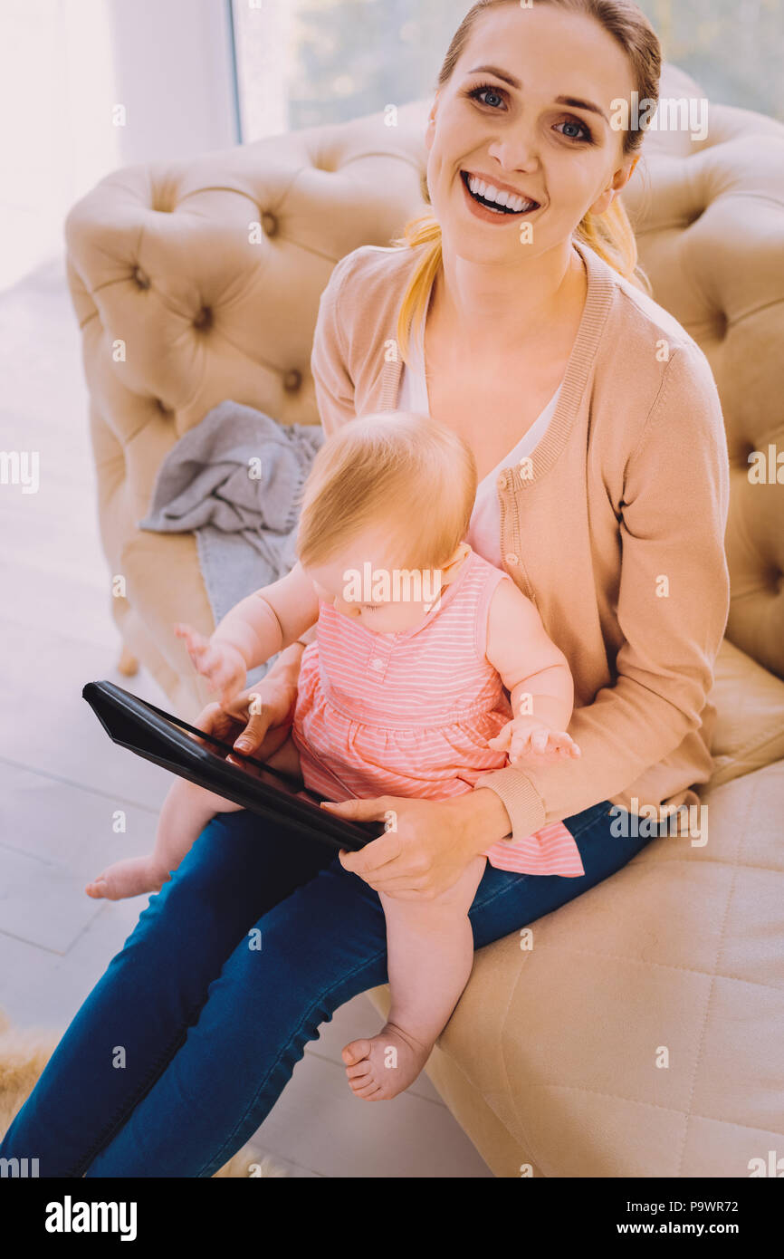 Smiling Baby sitter. Positive qualifizierte Babysitter lächelnd, während sie ein Baby im mit modernen Gerät Stockfoto